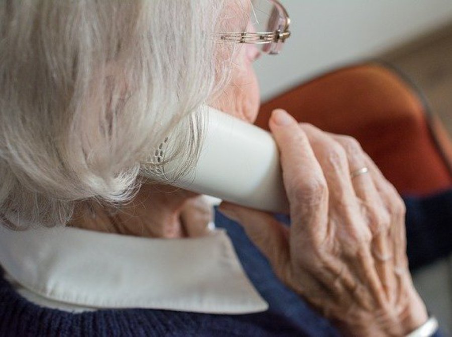 Ältere Frau mit Telefonhörer in der Hand in Sessel sitzend